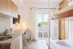 A modern hotel room with a kitchen area, a balcony with a view, and a bed with a neatly made white towel. - Mykonaki Hotel (Mykonos)