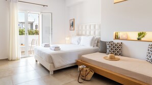 Camera d'albergo con un letto grande, un divano, un balcone con una sedia e uno scaffale a parete con oggetti decorativi.