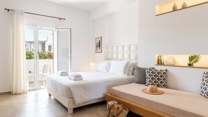 Une chambre d’hôtel avec un grand lit, un canapé, un balcon avec un fauteuil et une étagère murale agrémentée d’objets décoratifs.