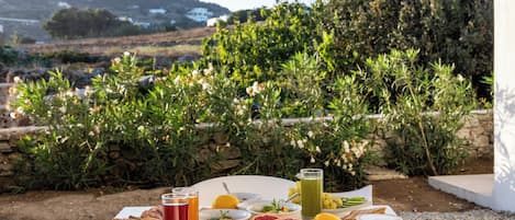A table set with breakfast items including bread, fruit, and beverages, with a scenic view of a mountainous landscape in the background.
