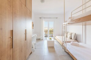 A modern, well-lit room with a bunk bed, a white desk, a chair, and a view of the outdoors through a large window. - Mykonaki Hotel (Mykonos)