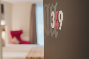 Interior de una habitación de hotel con una cama, un almohadón rojo y una pared con el número 349.