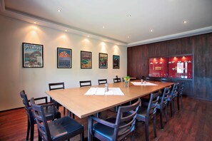 A conference room with a long table, chairs, framed pictures on the wall, and a red glass display case. - Boutique Hotel Waldegg (Horw)