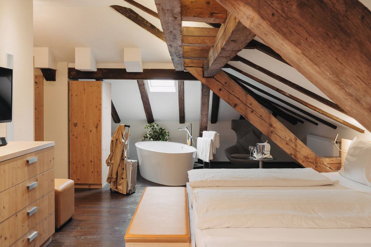 A bedroom with a large bed, a wooden dresser, a round bathtub, and a wooden ceiling structure.