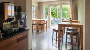 Una cocina moderna con cafetera, un comedor con mobiliario de madera y ventanas grandes con cortinas.