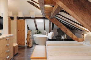 Ein Schlafzimmer mit einem großen Bett, einer Holzkommode, einer Badewanne und einem Holzbalkenbau.