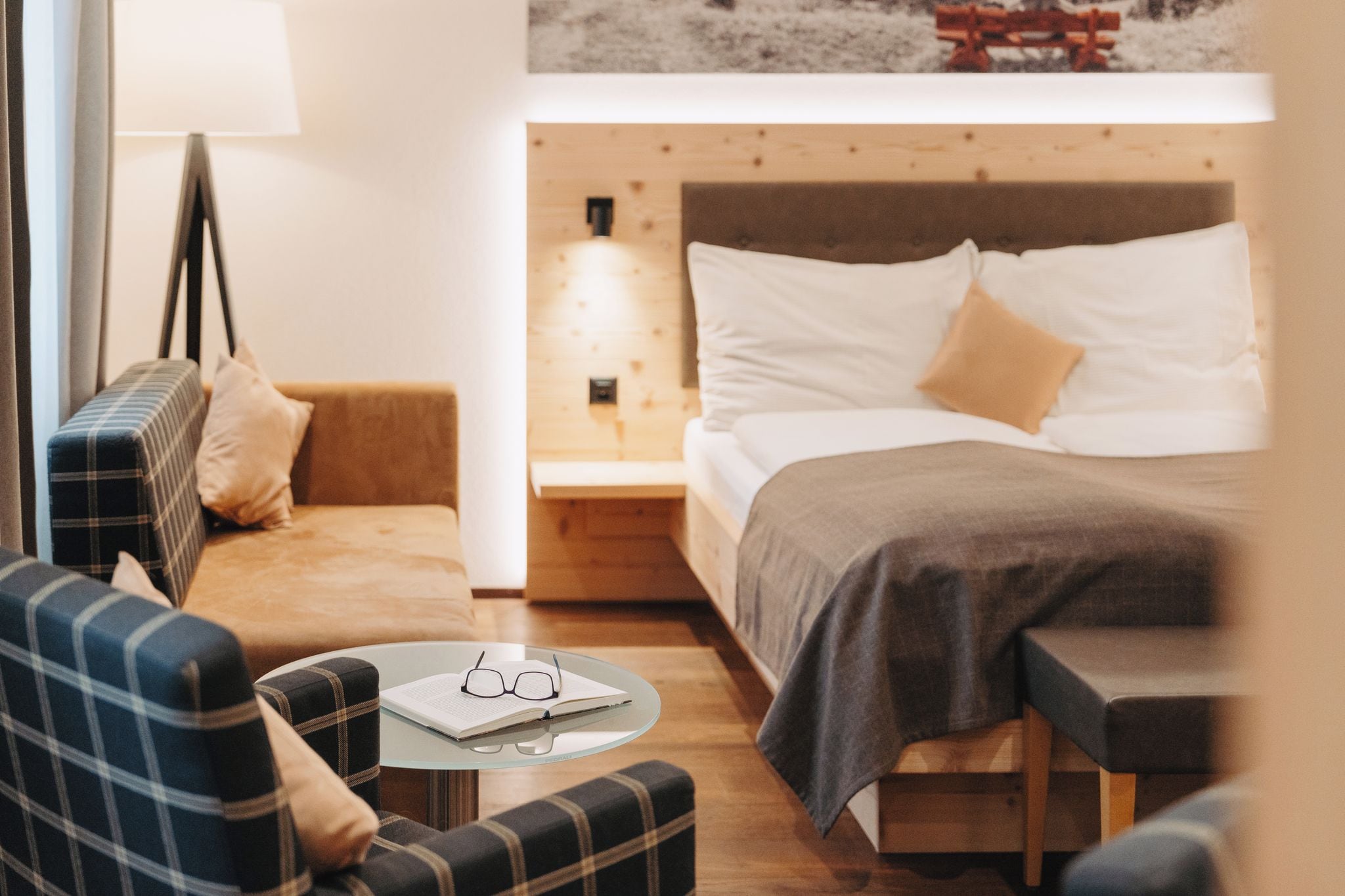 A cozy hotel room with a bed, a sofa, a small table with glasses, and a lamp.