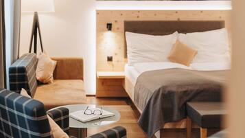 A cozy hotel room with a bed, a sofa, a small table with glasses, and a lamp.