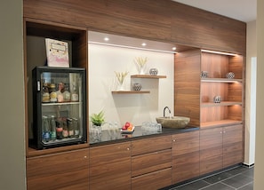 Eine moderne Küche mit Holzausstattung, einem Getränkekühlschrank mit Glastür, einem Waschbecken aus Stein und dekorativen Regalen.