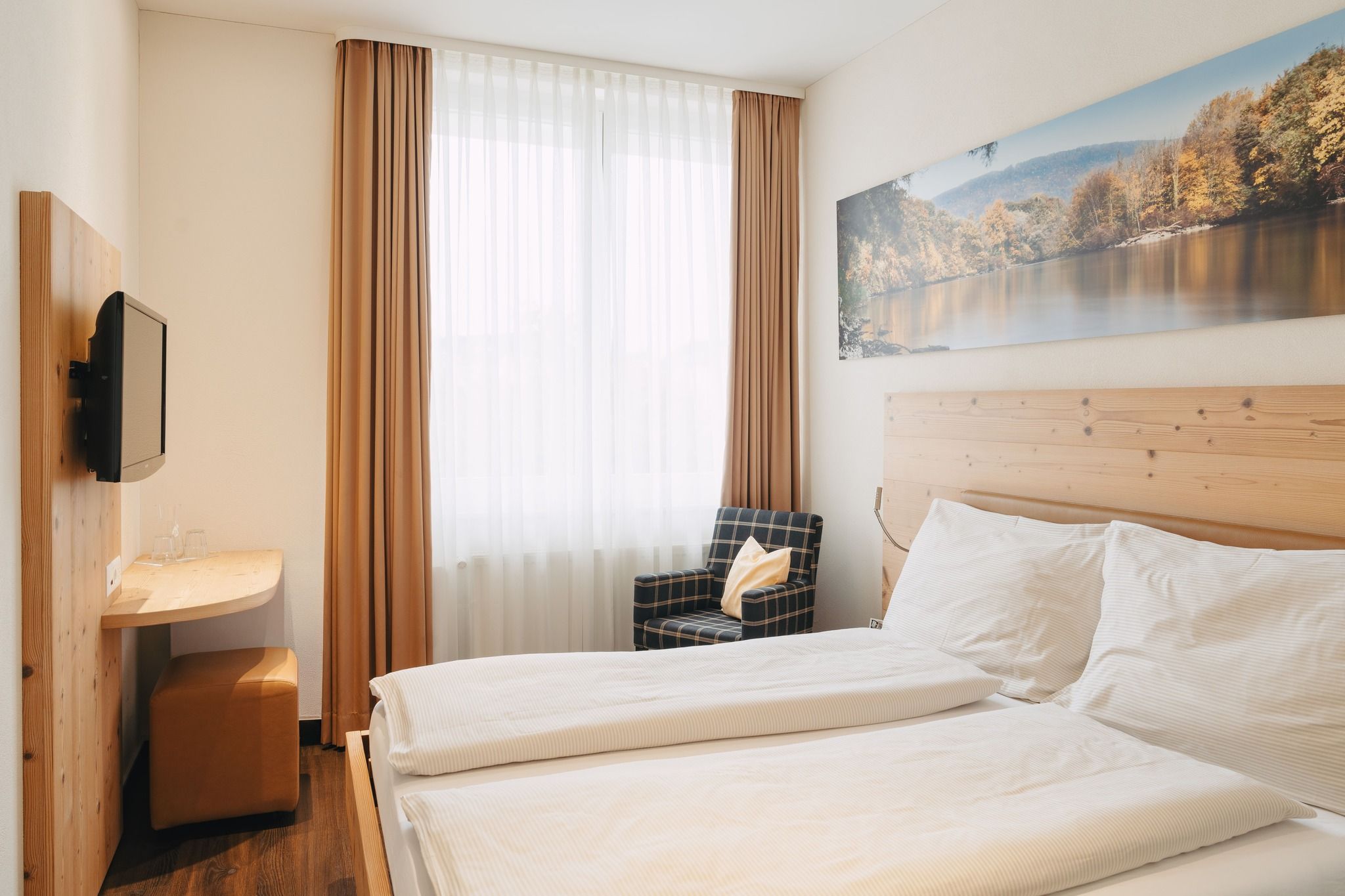 A hotel room with a bed, a chair, a small table, and a painting on the wall.