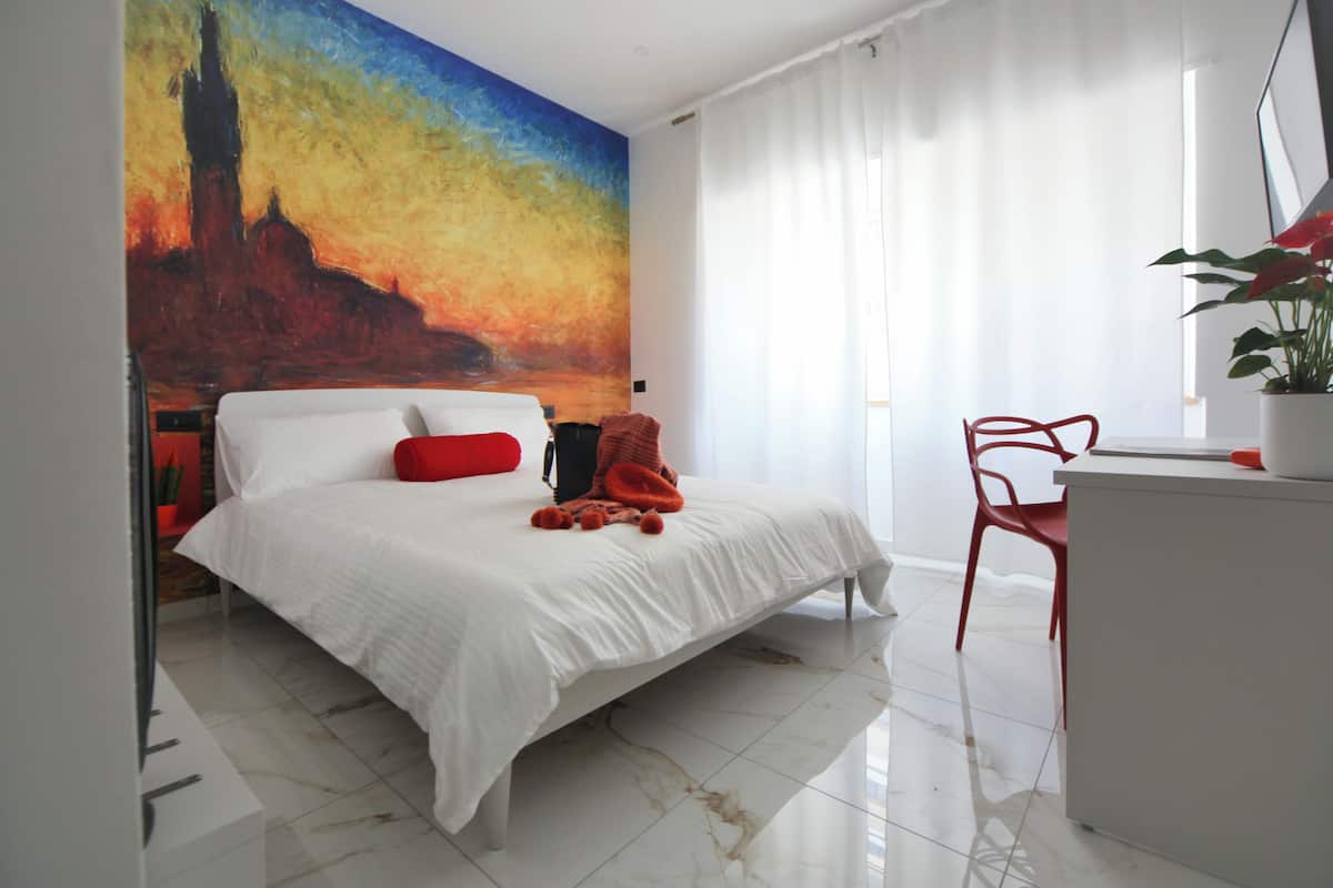 A modern hotel room with a large bed, a desk, a chair, and a vibrant mural on the wall.