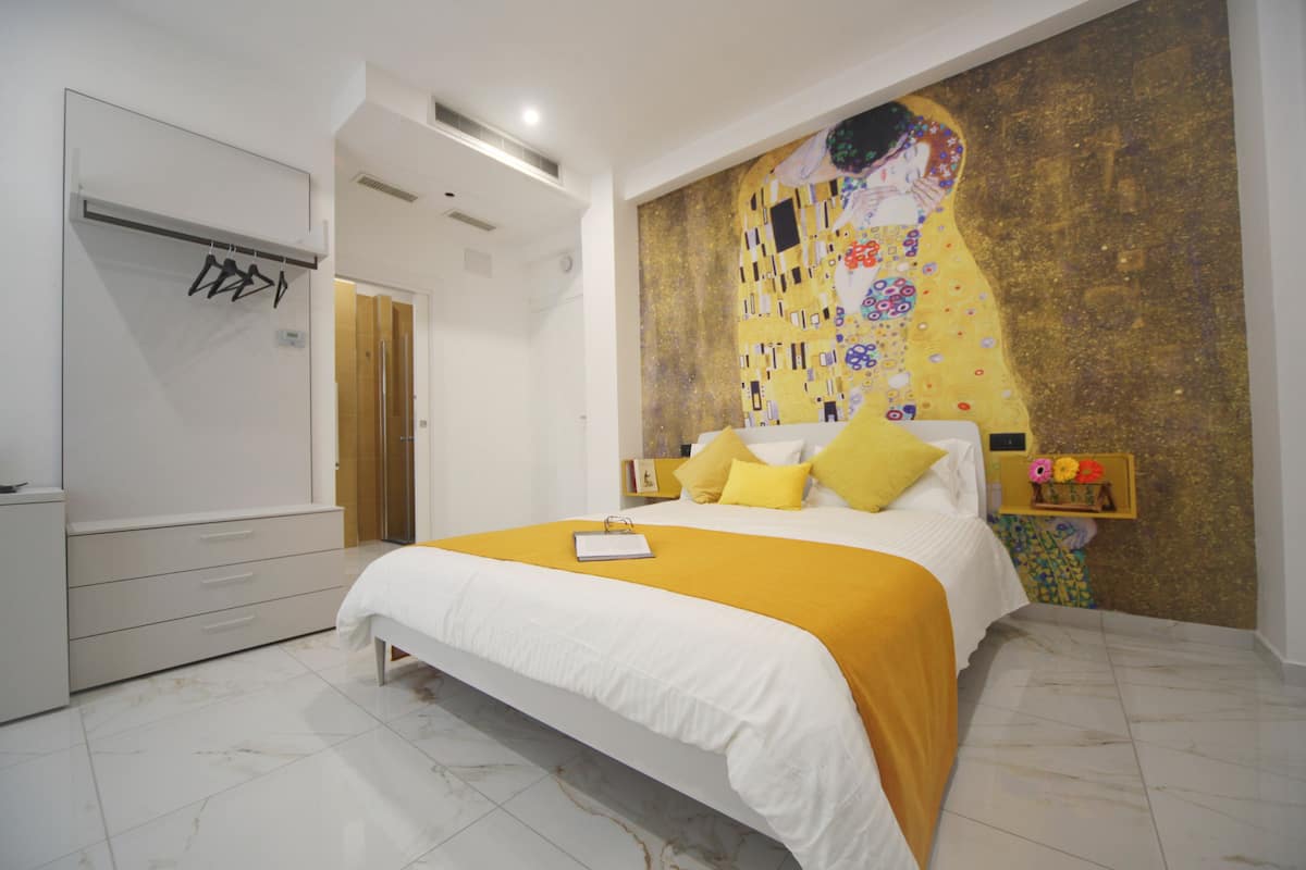 A modern bedroom with a large bed, a white wardrobe, and a mural on the wall.