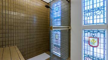 Bathroom features a glass shower enclosure with a showerhead, framed by a white border, and a stained glass window on either side.