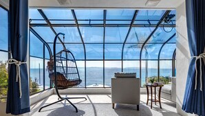 Ein Zimmer mit großem Fenster, einem Hängesessel, einer Couch und einem kleinen Tisch mit Büchern.