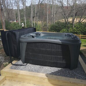 Relax in a serene outdoor hot tub surrounded by lush trees and a wooden fence.