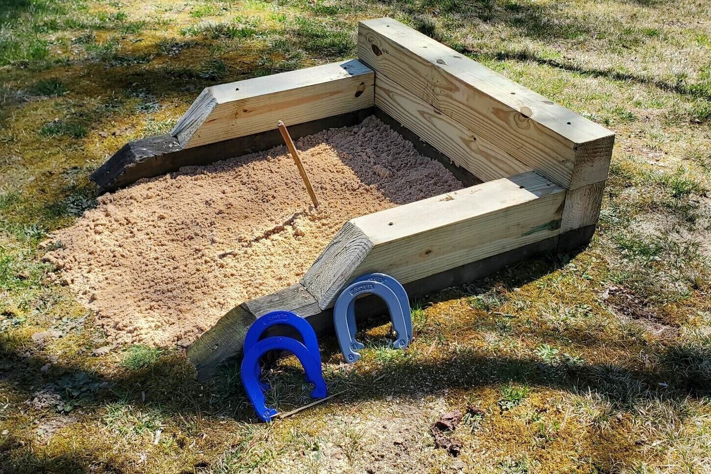Un arenero con borde de madera y dos herraduras azules en el suelo.