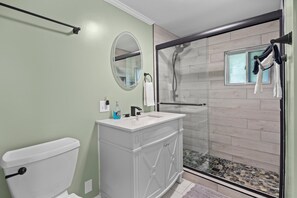 Features a sleek vanity, large mirror, toilet, and glass-enclosed shower area.