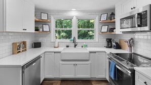 Una cocina moderna con armarios blancos, un lavamanos doble, horno empotrado y una ventana con vistas al verdor.