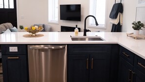 A modern kitchen with a large island, stainless steel dishwasher, and black cabinets.