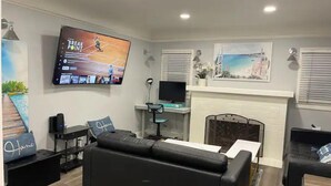 A living room with a black leather sofa, a flat-screen TV, a fireplace, and a painting above it. - House-view & 5 min Walk to Beach (Hermosa Beach)