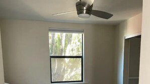 A small bedroom with a single bed, a ceiling fan, a window with a view of trees, and a closet. - Large 1BR1BA with ocean view+walking to downtown (Sausalito)