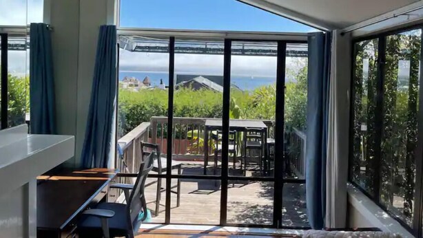 A modern room with a large sliding glass door leading to an outdoor patio with a view of the sea and buildings. - Large 1BR1BA with ocean view+walking to downtown (Sausalito)