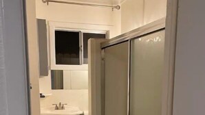 Un pasillo estrecho con un baño que incluye inodoro, lavabo y zona de ducha.