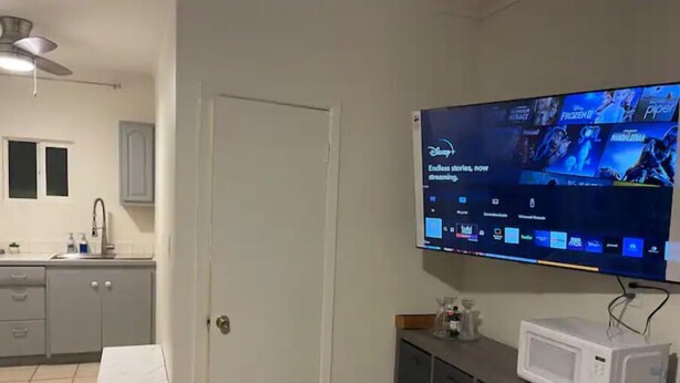 Sala de estar con televisor de pantalla plana mostrando contenido de Disney+, un microondas en un mueble y una mesita.