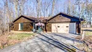 Eine zweigeschossige Holzhütte mit Garage, überdachter Terrasse und Auffahrt.