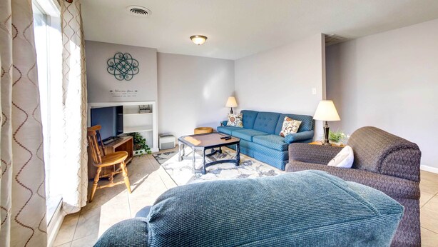 Ein Wohnzimmer mit einem blauen Sofa, einem grauen Sessel, einem Holzstuhl, einem Couchtisch und einer Lampe.