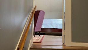 Un escalier menant à une chambre à coucher qui contient un lit, une chaise et un petit tapis.