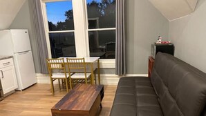 Un espace de vie compact comprenant un canapé, une table à manger avec des chaises, un petit coin cuisine et une grande fenêtre.