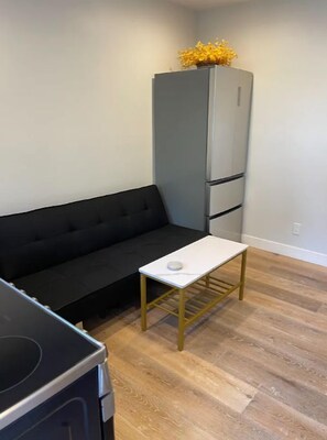 A compact living space with a black sofa, a small white table, a grey refrigerator, and a black stove.