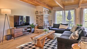 Una sala de estar acogedora con televisor, muebles de madera, chimenea y ventanas amplias.