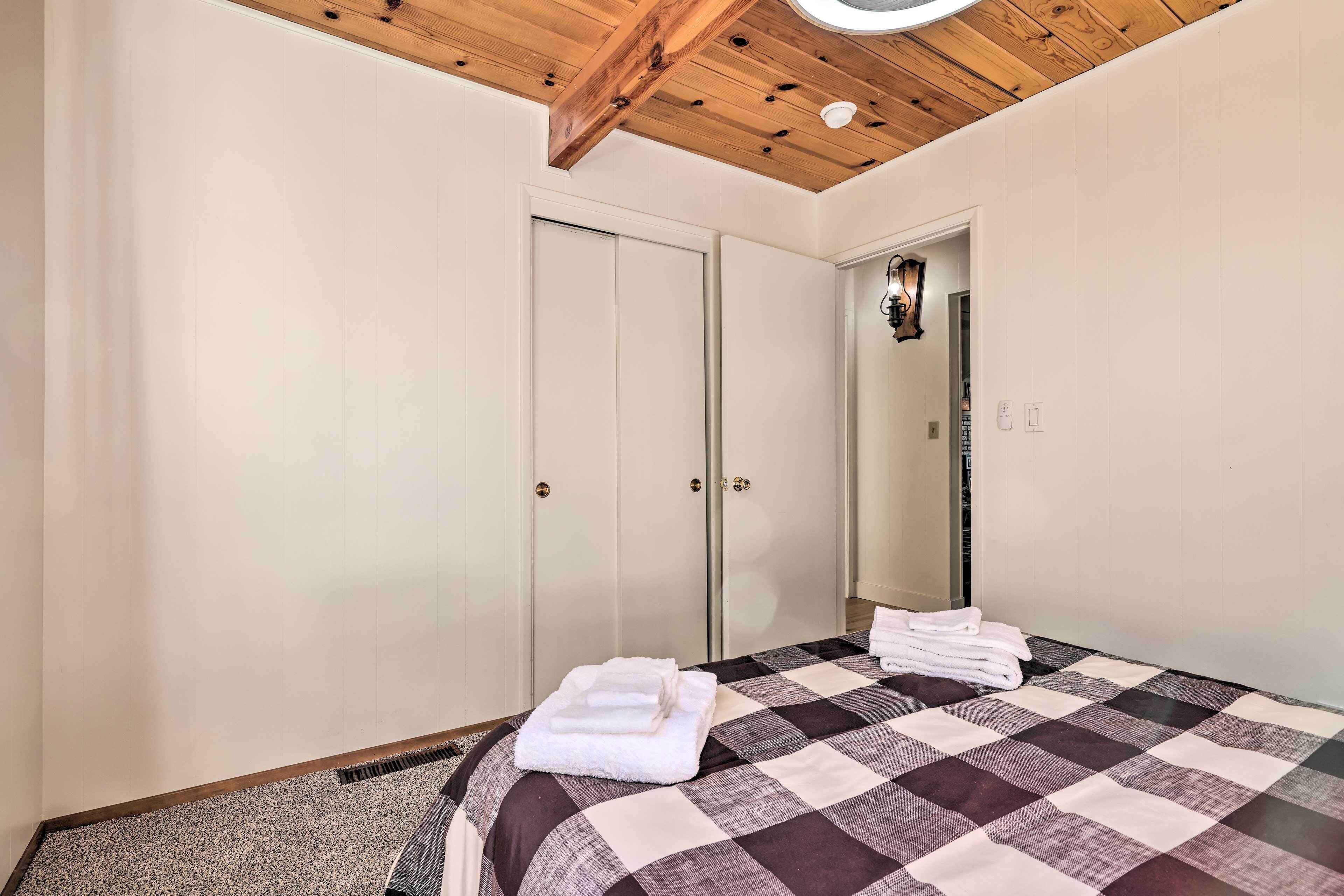 Un dormitorio con colcha a cuadros, dos puertas blancas, techo de madera y un espejo en la pared.