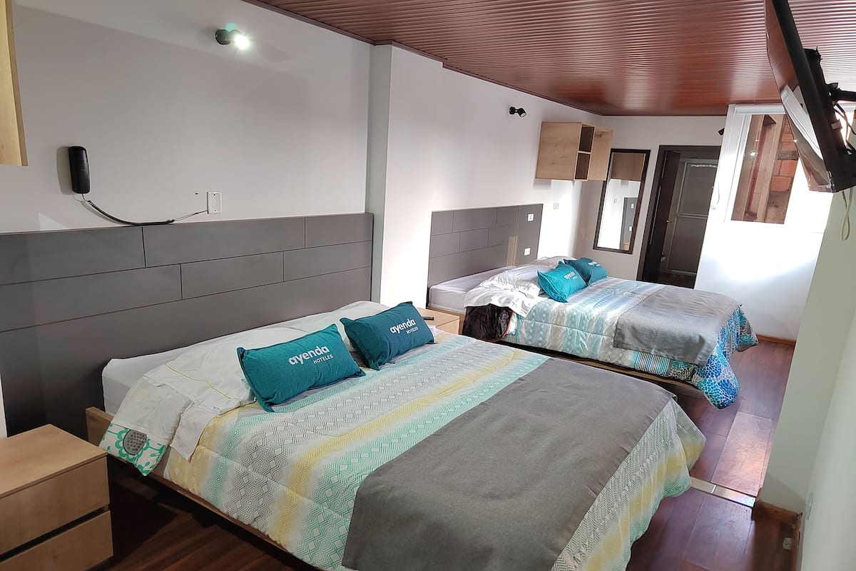 Een hotelkamer met twee bedden, elk voorzien van beddengoed en kussens met een patroon, een houten hoofdbord, een nachtkastje en een aan de muur bevestigd telefoontoestel.