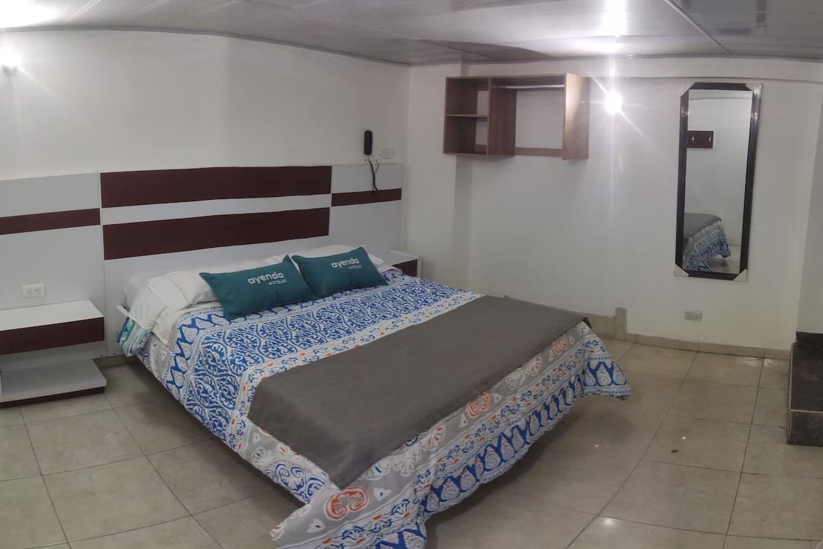 Een slaapkamer met een bed, nachtkastje, spiegel en plank.