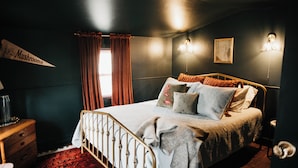 A bedroom with a bed, a nightstand, a lamp, and a window with curtains.
