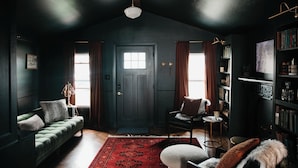 A dark-themed living room with a green sofa, a chair, a bookshelf, and a door with windows.