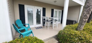 A covered patio with a table and chairs, a blue chair, and a small garden area. - Perfect Getaway – Beach Access, Pool & Hot Tub (Destin)