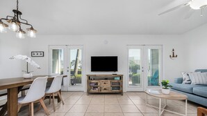 A modern living room with a wooden dining table, white chairs, a TV, and a blue sofa.