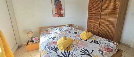 A bedroom with a bed, a wooden wardrobe, a bedside table with a lamp, and a framed picture on the wall.