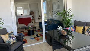 Uma sala de estar moderna com uma porta de vidro que dá para uma área de jantar. Há dois sofás, uma mesa de centro e um vaso de planta.