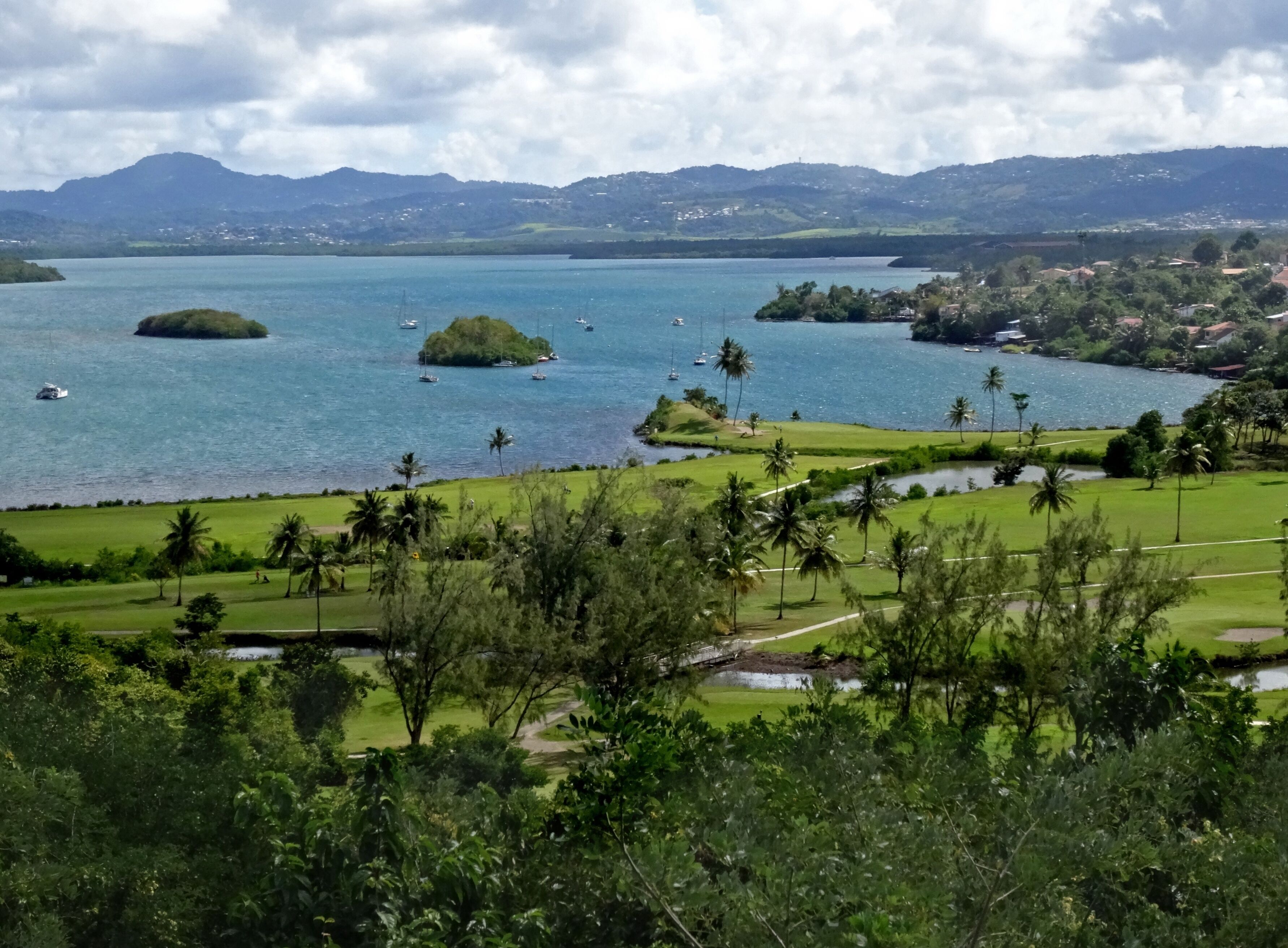 A coastal landscape with a golf course, a lake, and distant mountains.