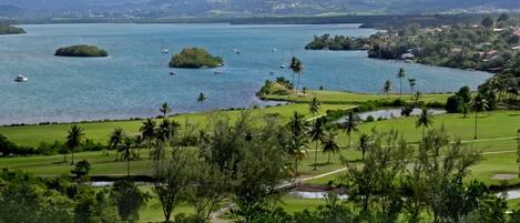 A coastal landscape with a golf course, a lake, and distant mountains.