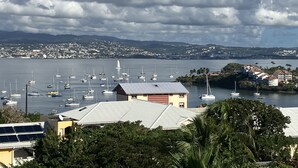 Marina com vários veleiros atracados, uma vila costeira ao fundo e um edifício com telhado inclinado em primeiro plano.