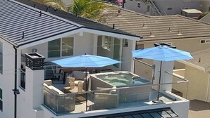 Un edificio moderno con balcón de vidrio, mobiliario exterior y una bañera de hidromasaje.