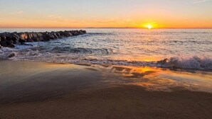 Ein Strand mit Wellen bei Sonnenuntergang, felsigem Ufer und bewölktem Himmel.