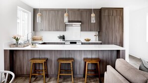 Eine moderne Küche mit einer großen Kochinsel, Holzbarhocker und Pendelleuchten.