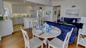 Une cuisine moderne avec des meubles blancs, un coin repas avec une table ronde et des chaises blanches, et un canapé bleu foncé dans l’espace salon.